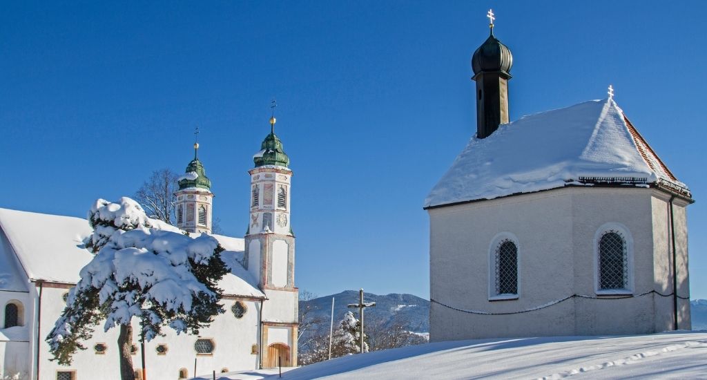 small chapel on the right and larger church on the left, covered with a thick layer of snow on a sunny winter day