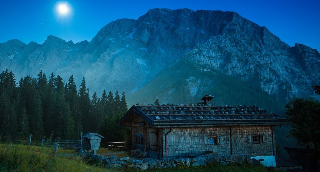 An old farm barn on a meadow in the Bavarian alpes near Berchtesgaden Bavaria at night with the moon shining on the night sky