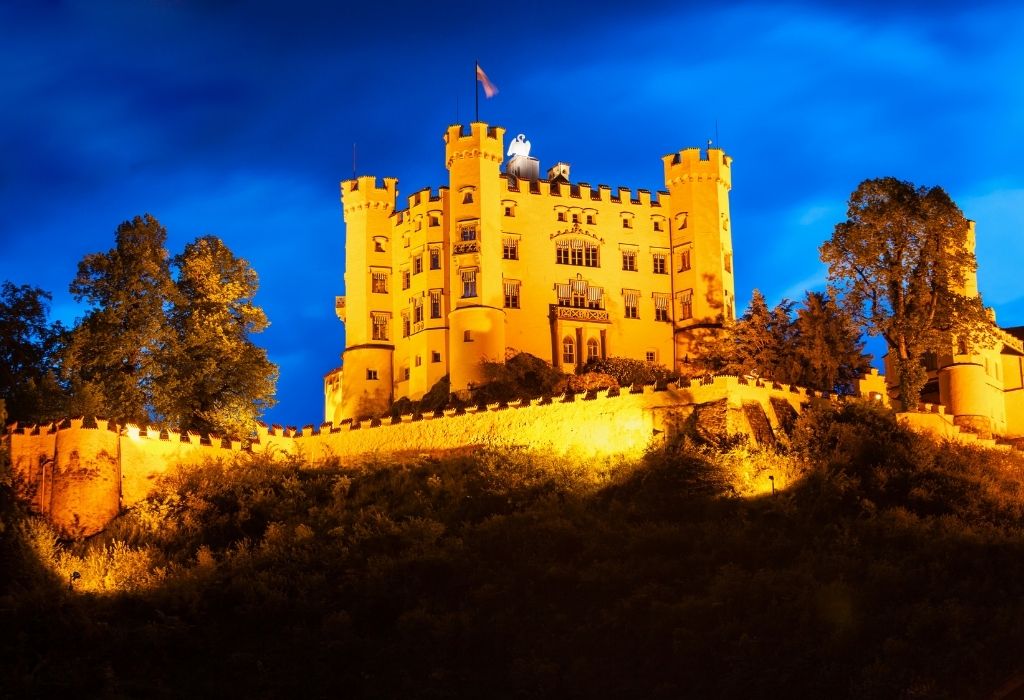 Hohenschwangau Castle lid up with lights, shining orange during blue hour 