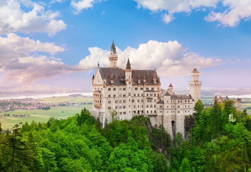 Neuschwanstein Castle - a large white fairytale castle on top of a wooded hill near Füssen