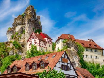 Halftimbered houses with red tiled roofs perched on a steep mountain with a large rock formation towering over the village - Tuchersfeld Bavaria